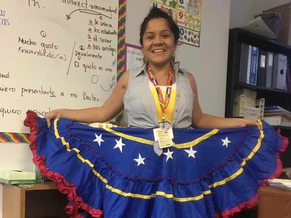 Paola Branda sonriendo en su salón de clases con materiales culturales venezolanos